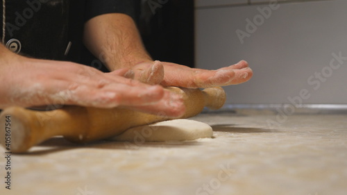 Close up arms of cook unrolling pastry using rolling pin on a kitchen table at restaurant. Male hands of chef rolling out dough on a wooden surface at cuisine. Process of making pizza. Slow motion