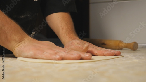 Male arms of cook forming pastry on a wooden surface at restaurant. Hands of chef shaping floured dough for pizza on a kitchen table at cuisine. Concept of preparing food. Close up Slow motion