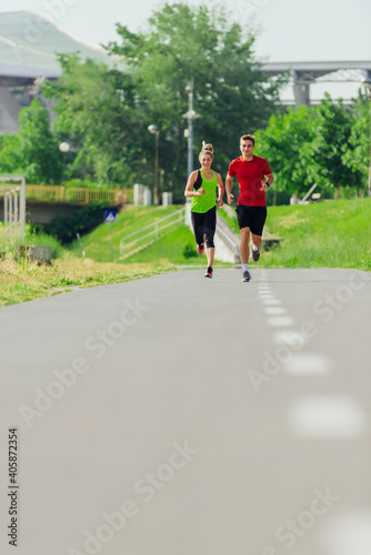 Young male and female athletes jogging and running on a road in the park. © qunica.com