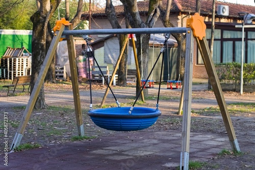 A wooden swing with a circular blue rubber seat in a public park (Pesaro, Italy, Europe)