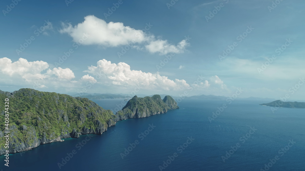 Obraz premium Hilly islands at blue ocean coast aerial view. Nobody nature scenery of Palawan, El Nido Isles, Philippines. Green tropic forest at mount ranges under fluffy clouds on sky. Cinematic drone shot