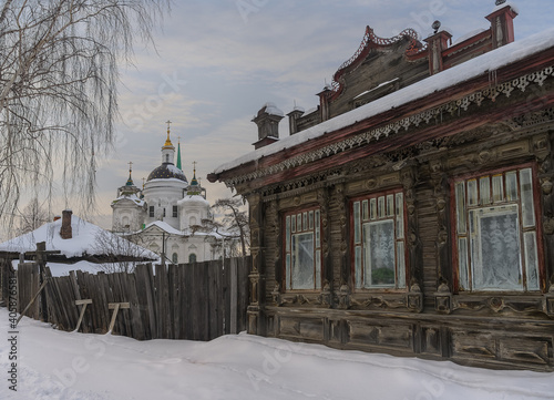 view of the old rural church in the historic village of Byngi (Nevyansk region, Russia) in winter. in the foreground is one of the carved wooden houses of this village with a rickety fence