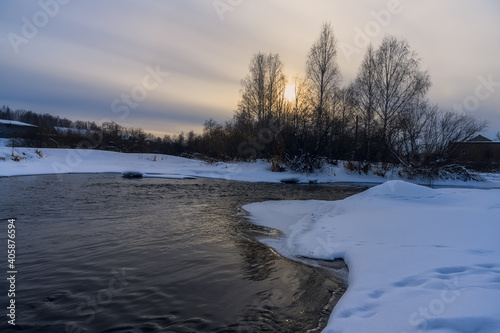 winter landscape with a river. evening on the Neiva River (Russia). white snow lies on the banks. the sun will soon sink below the horizon. sunlight is reflected in the water. yellow clouds