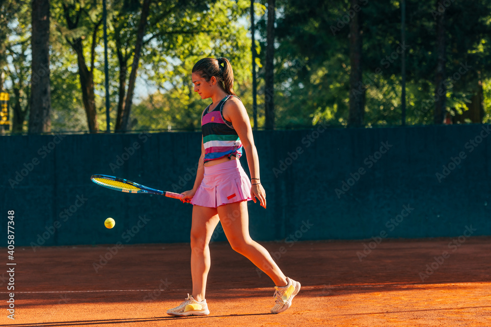 Young female tennis player hitting the ball to the ground with a racket while waiting for the tennis game to start