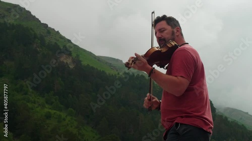 Low angle view of man playing violin standing in mountain valley. Music connected with nature photo