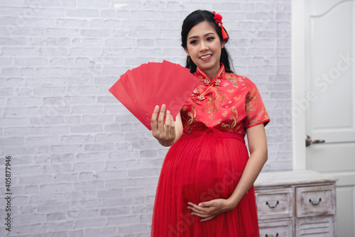 Pregnant asian woman with Chinese traditional dress cheongsam or qipao holding ang pow or red packet monetary gift. Chinese new year concept