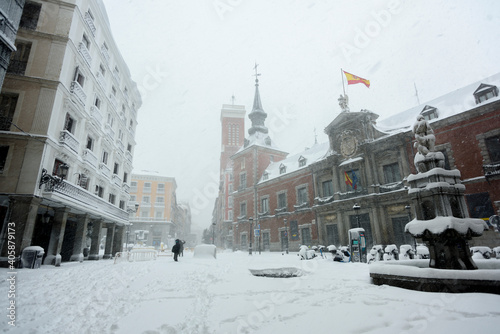 View of the Plaza de Santa Cruz in Madrid covered with snow under a heavy snowfall.