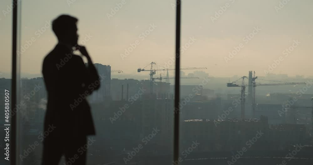 Successful businessman thinking about future company plans investment deals looking through window of high skyscraper office building.