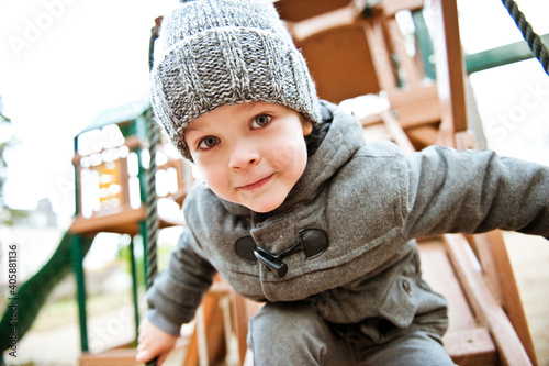 A cute preschooler boy in a knitted hat is playing in the Playground on an autumn day.