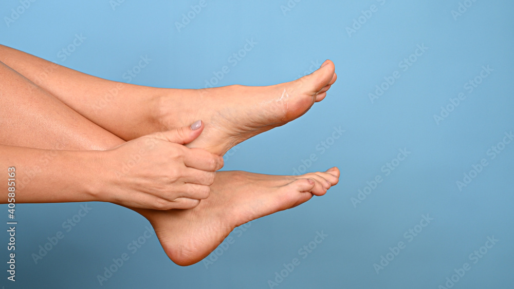 Woman massaging her tired feet. Close-up of female feet on blue background with copy space. Leg health and body care concept. Woman massaging her tired feet. Close-up of female feet on blue background with copy space. Leg health and body care concept.