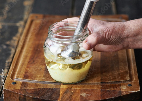 Whisk homemade mayonnaise with olive oil and eggs. Combine the sauce ingredients. Step by step preparation of mayonnaise at home. Female hands are holding a blendar.