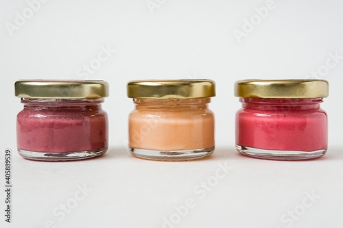 Three jars of various fruit jam standing in a row on white background.
