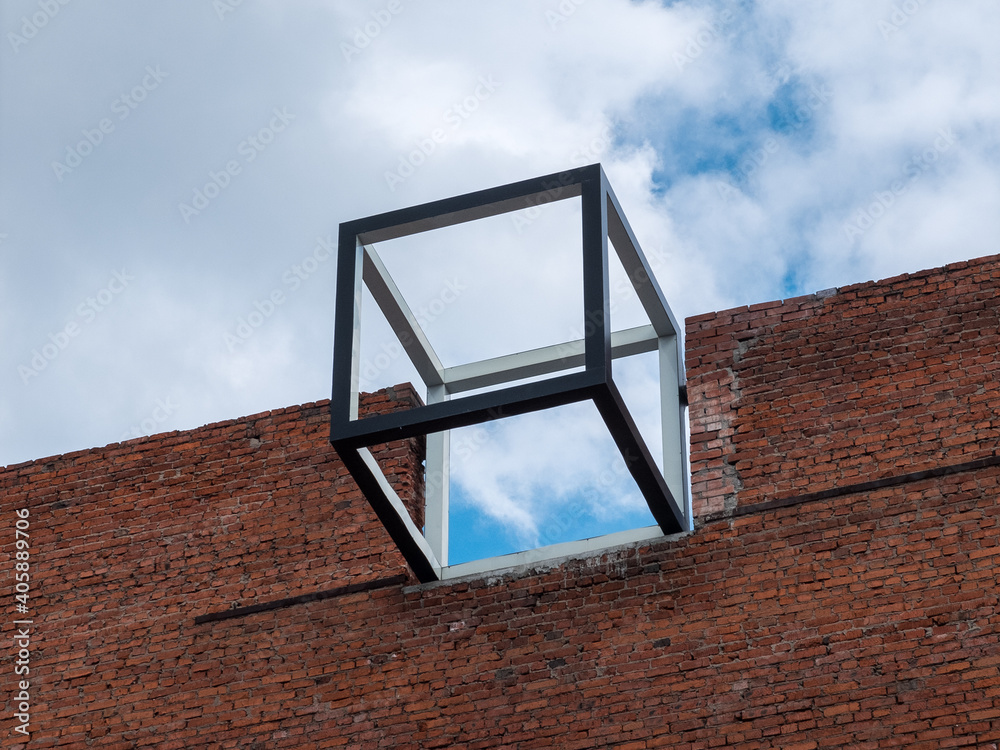 A frame cube installed on the roof of a brick building. Modern urban design element.