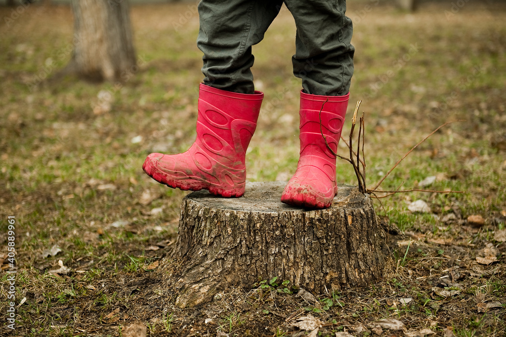 A child in bright rubber boots stands on a stump.