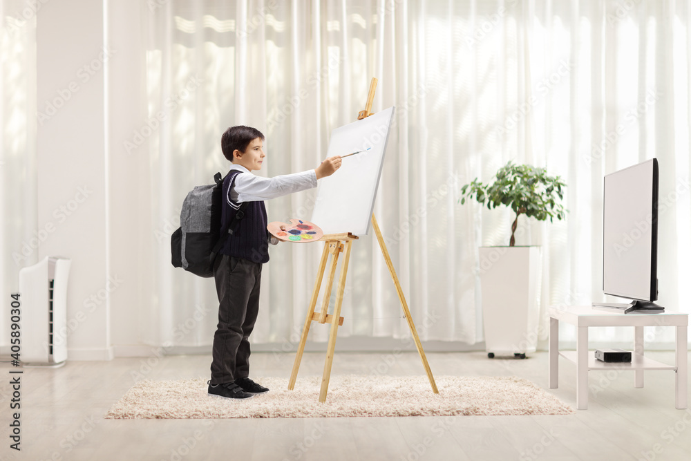 Schoolboy using an easel and painting on a canvas