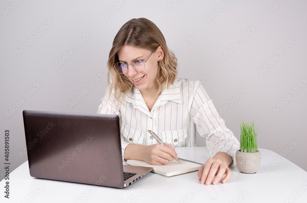 Young woman using laptop smiling and writing something in a notebook Young woman using laptop smiling and writing something in a notebook