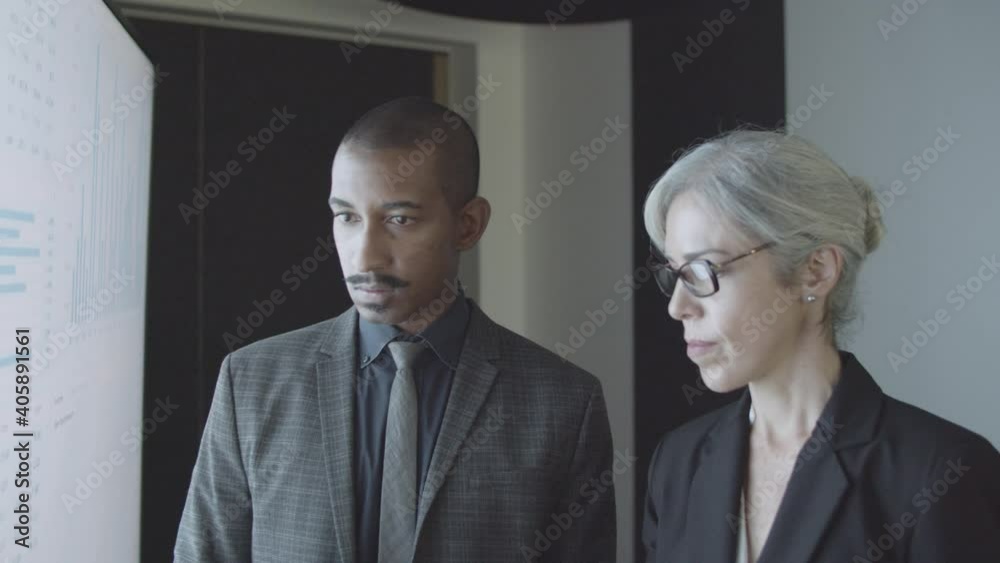 Black financial advisor explaining stock market statistics to client. Diverse couple of businesspeople analyzing financial charts at big presentation screen, pointing at diagrams. Investment concept Black financial advisor explaining stock market statistics to client. Diverse couple of businesspeople analyzing financial charts at big presentation screen, pointing at diagrams. Investment concept