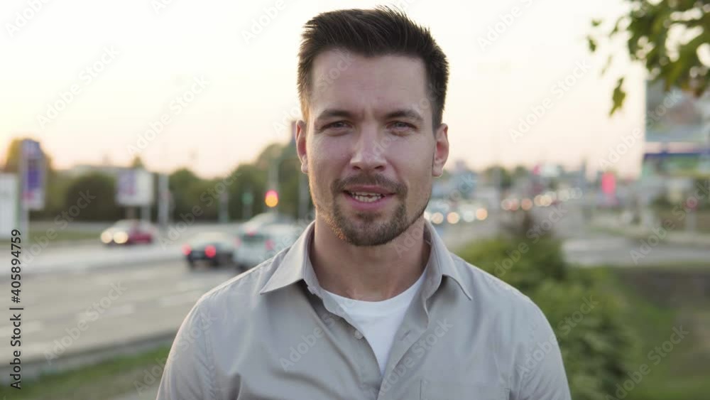 A young Caucasian man talks to the camera with a smile in an urban area - closeup - a busy intersection in the blurry background A young Caucasian man talks to the camera with a smile in an urban area - closeup - a busy intersection in the blurry background
