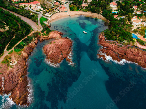 Aerial view of a small beach with turquoise waters, anchored small boat and red rocks, typical of the Esterel close to Cannes. picture taken in Agay, French Riviera, Côte d'Azur south of France