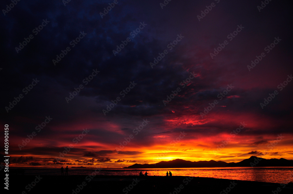 Fototapeta premium Stunning and colourful sunset with overcast sky over the Indian Ocean with silhouette of an island and reflection on the sea. Seychelles