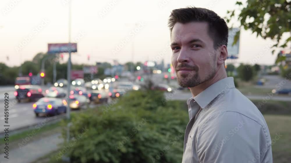 A young Caucasian man turns and smiles at the camera in an urban area - a busy intersection in the blurry background A young Caucasian man turns and smiles at the camera in an urban area - a busy intersection in the blurry background