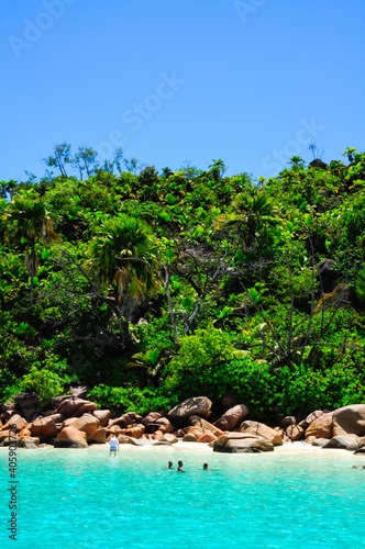 Anse Lazio with rocky granite pink coastline with people swimming in the water in the summer