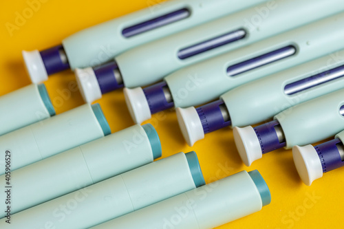 Top and bottom ends of self applying medication syringe pen filling the frame on seamless yellow backdrop. Studio medical equipment still life concept with auto-injector disposable devices.