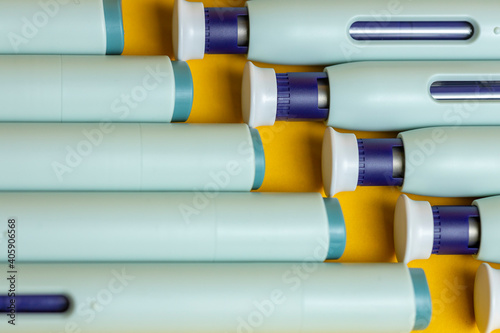 Closeup of top and bottom ends of self applying medication syringe pen filling the frame on seamless yellow backdrop. Studio medical equipment still life concept with auto-injector disposable devices.