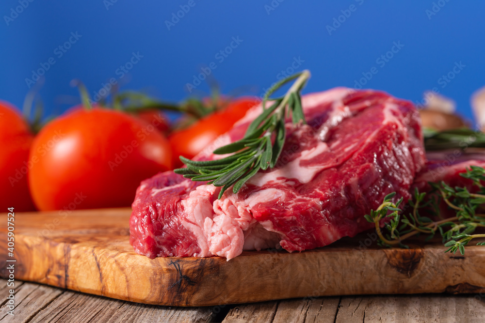 Raw beef meat with tomatoes and rosemary on wooden cutting board o blue background. Image for butcher shop. Appetizing view for advertising.