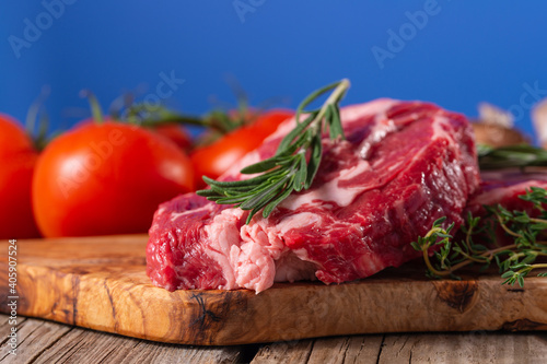 Raw beef meat with tomatoes and rosemary on wooden cutting board o blue background. Image for butcher shop. Appetizing view for advertising.