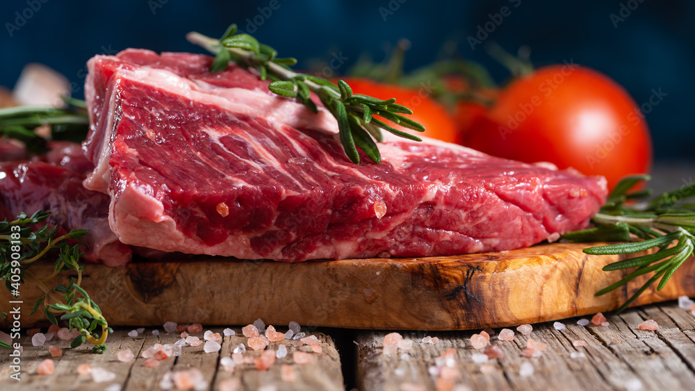 Raw pork or beef meat with tomatoes and rosemary on wooden cutting board o blue background. Image for butcher shop. Macro shot.