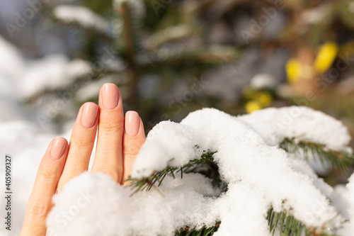 Beautiful professional nude beige manicure on a female hand against the background of a snow-covered Christmas tree on a sunny day in natural light © Анастасия Каргаполов