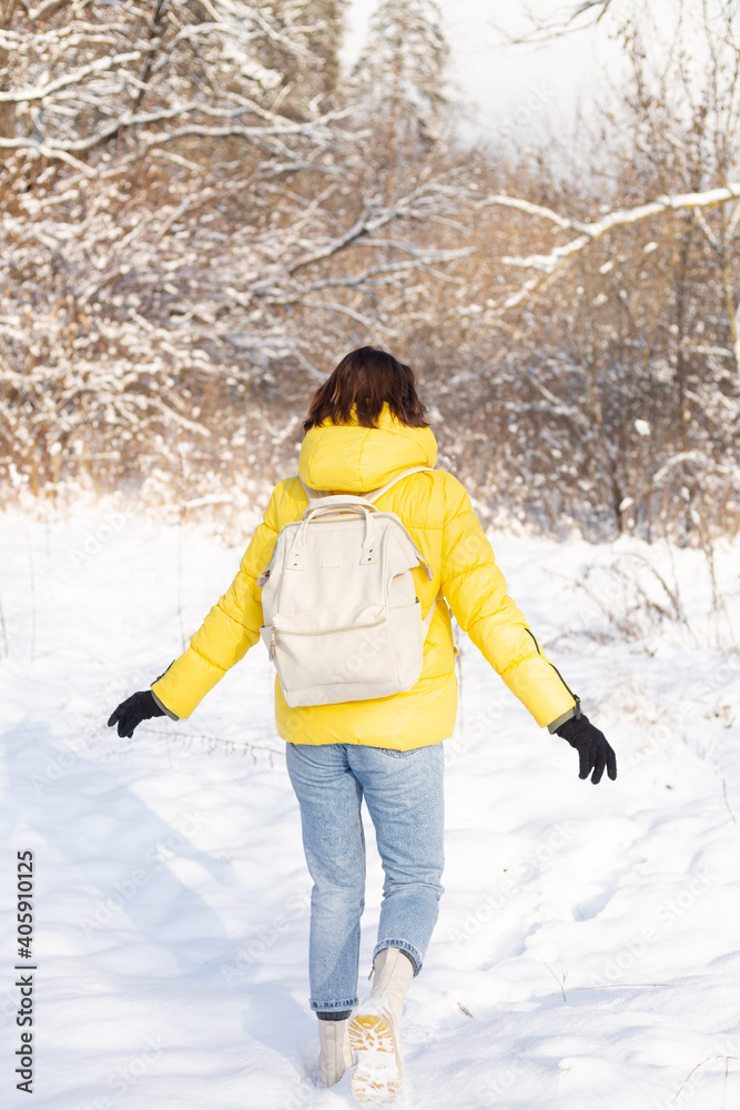 Back view of a woman in a bright yellow jacket and jeans with a backpack in a snowy landscape forest walks through the snowdrifts Back view of a woman in a bright yellow jacket and jeans with a backpack in a snowy landscape forest walks through the snowdrifts