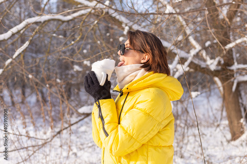Beautiful young cheerful woman in a snowy landscape winter forest in sunglasses with a cup filled with snow having fun © Анастасия Каргаполов