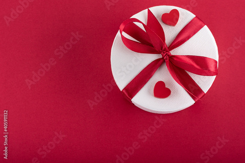 Gift with a red ribbon and two red hearts on a red background. Concept Valentine's day. Concept mother's day. Free copy space