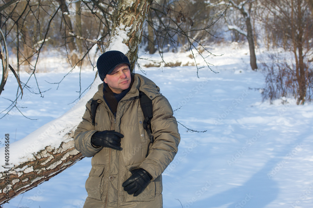 A man in winter clothes. Stands with a pensive look in a winter park. There is a lot of snow around.