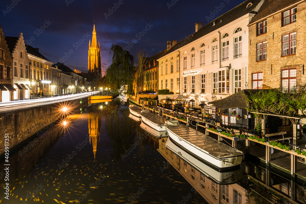 Boats on river Dijver and Church of Our Lady (Onze-Lieve-Vrouwekerk) from Koningsbrug (King’s Bridge) in the centre of Bruges in Belgium during night.
