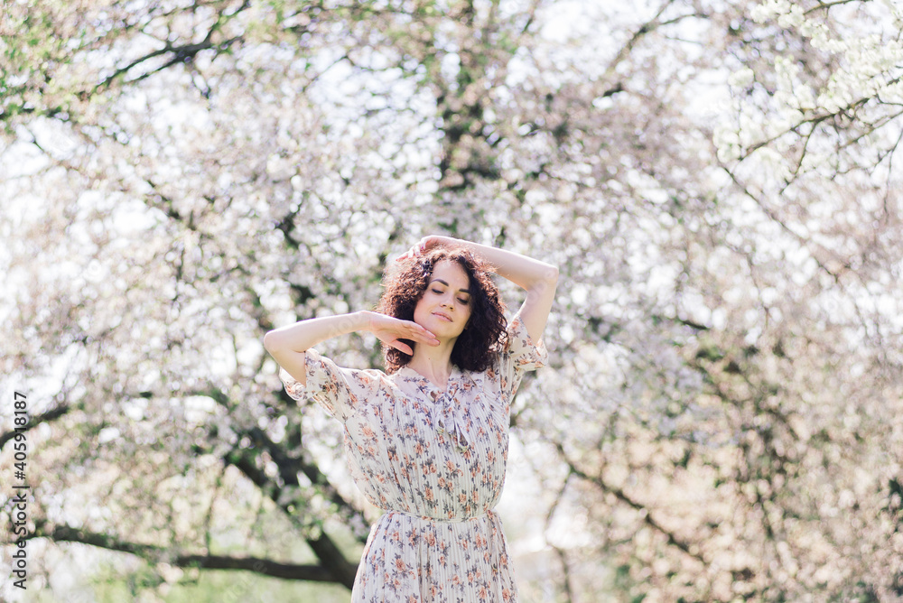 Young attractive woman with curly long hair posing in spring blooming garden, apple trees Young attractive woman with curly long hair posing in spring blooming garden, apple trees