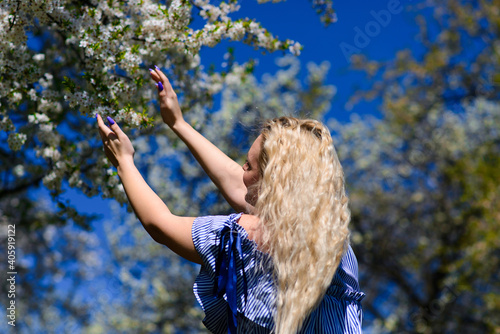 Blonde female looks at blue sky and reaches for sky with hands. Beautiful female admires nature.