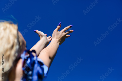 Blonde female looks at blue sky and reaches for sky with hands. Beautiful female admires nature.
