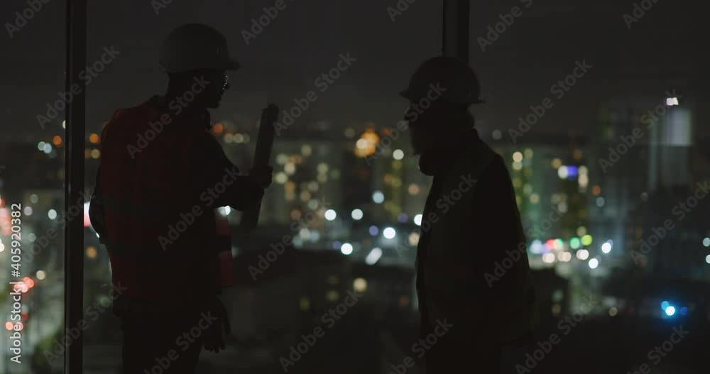 Couple of friendly workers standing in new building skyscraper near window observing beautiful city lights discussing plans. Construction coworkers.