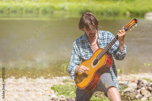 Adult male musician in a plaid shirt is playing the guitar on nature. Bright, sunny day, summer, outdoors. Close-up soft light portrait. Retro concept.