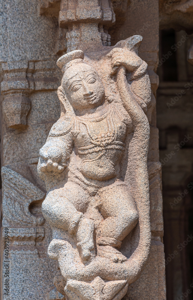 Hampi, Karnataka, India - November 5, 2013: Vijaya Vitthala Temple. Closeup of Beige stone statue of gracious smiling woman with snake. 