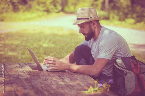 A young guy works on a laptop sitting at a wooden aged table. Concept of travel.
