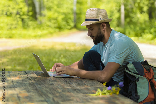 A young male working on laptop outdoors sitting at the wooden antique desk. Concept of travel, freelance, business.