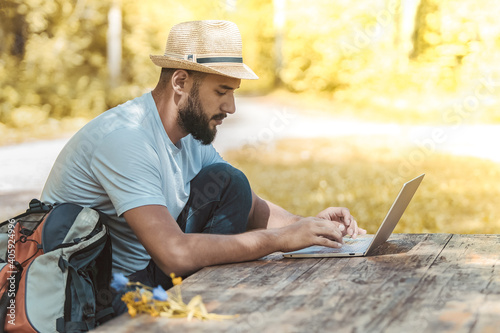 A young man is looking and working on laptop outdoors sitting at the wooden antique desk. Concept of travel, freelance, business.