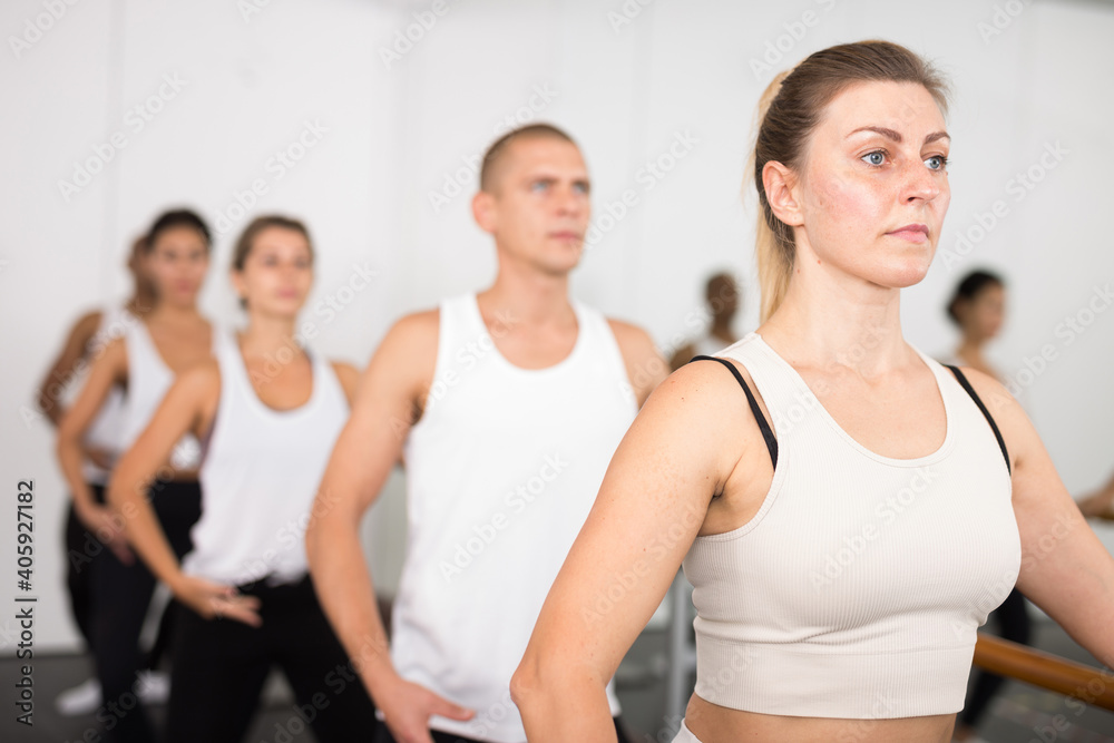 Group of people doing exercises using barre in gym with focus to fit athletic toned ..woman in foreground in health and fitness concept
