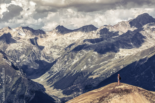 A traveler with a backpack stands on a cliff of huge mountains. Picturesque landscape with clouds. Travel concept.