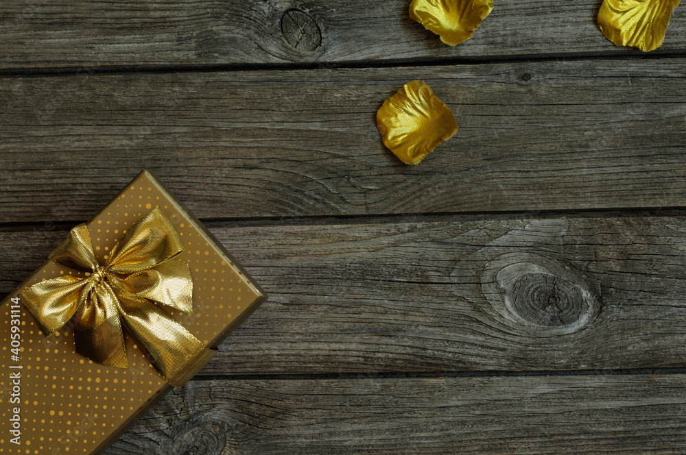 Gift box of golden color with a bow and shiny petals on a vintage table. Selective focus. Top view. Copy space