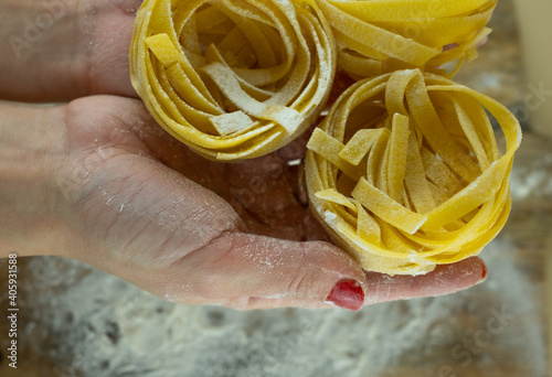 Female hands with pasta on wooden kitchen table, powdering by flour.